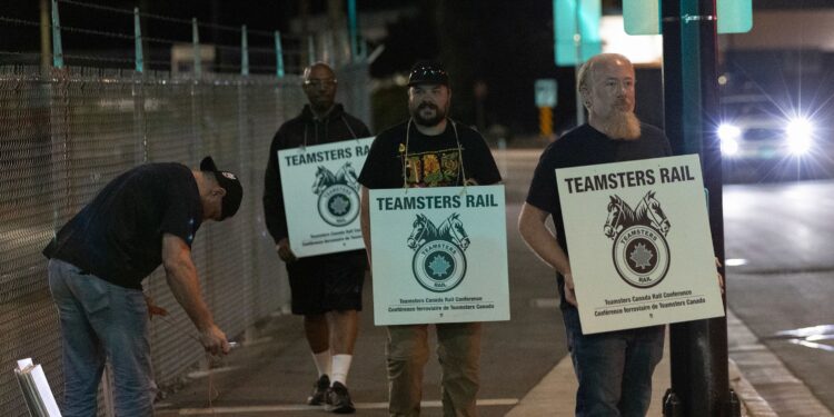 (Andrew Chin/Getty Images via CNN Newsource) Teamsters union members hold picket signs at the entrance of CN Rail Lynn Creek Yard in North Vancouver, British Columbia, Canada.