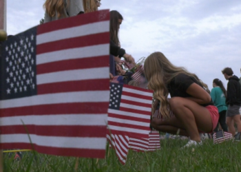 Under a US flag at half mast, students at Marquette Senior High School honored the victims of the 9-11 attacks by planting American flags in front of their school this morning.